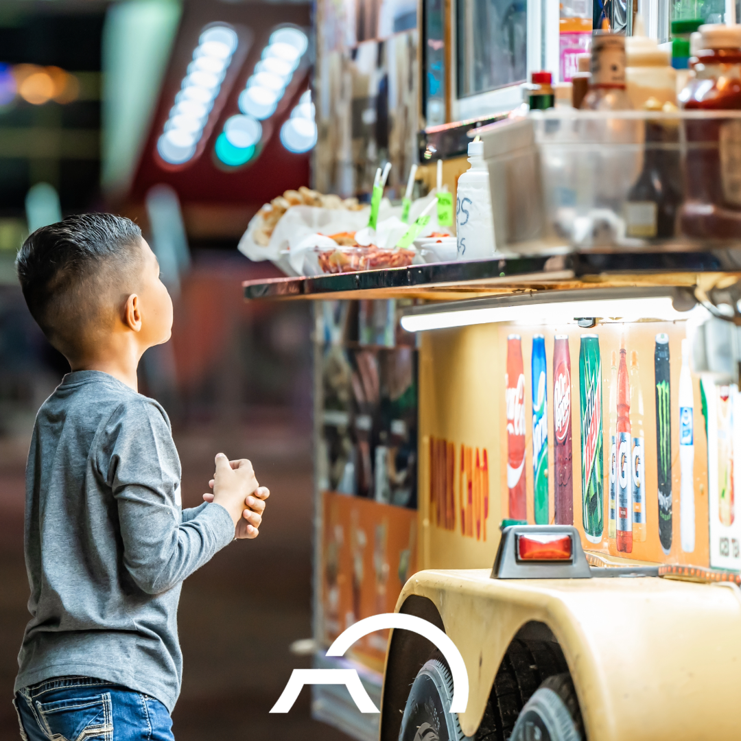 A young boy at the Howard County Fair stands eagerly in front of a food cart.